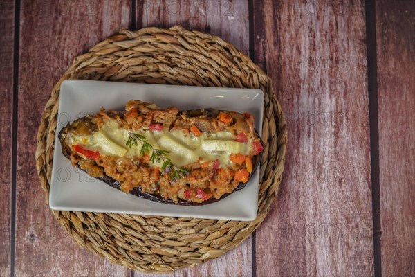 Eggplants stuffed with meat and vegetables on a white plate on a wooden table with a branch of rosemary in bloom