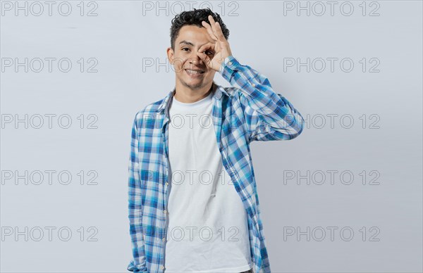 Happy young man making ok gesture with hand looking through fingers. Friendly man making ok gesture looking through fingers. Teenage guy making ok gesture looking through fingers