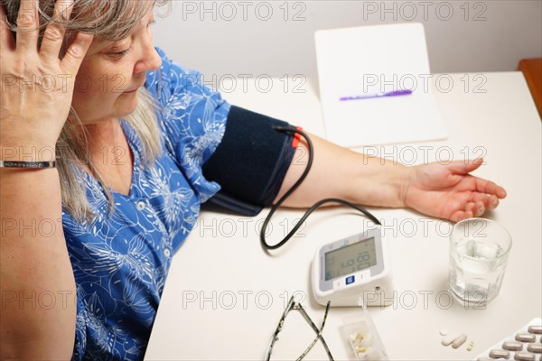 Older white-haired woman with glasses taking her blood pressure at home with white background