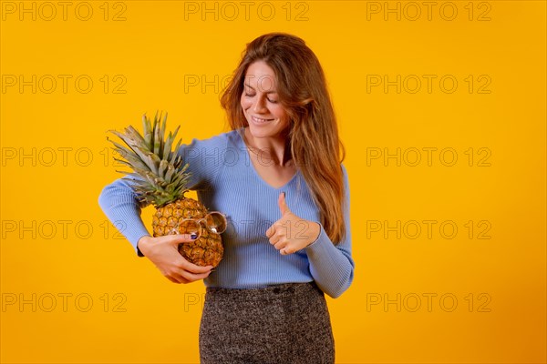 Woman with a pineapple in sunglasses in a studio on a yellow background