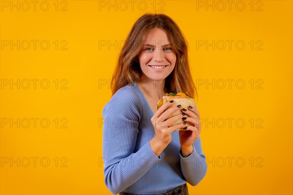 Portrait of woman eating a sandwich on a yellow background