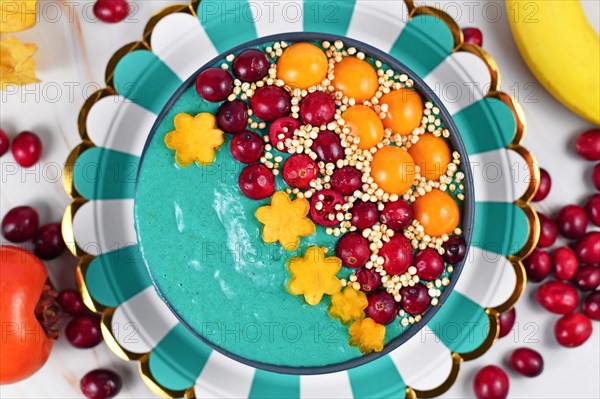 Top view of healthy yogurt and fruit smoothie bowl with natural green spirulina powder decorated with cranberries