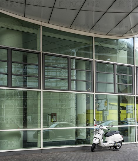 White Vespa scooter in front of glass facade of an office complex