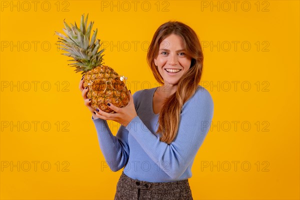 Girl smiling with a pineapple in sunglasses in a studio on a yellow background