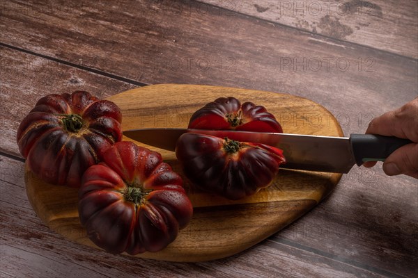 Close-up of a woman's hand with knife cutting tomatoes on a board on wooden table