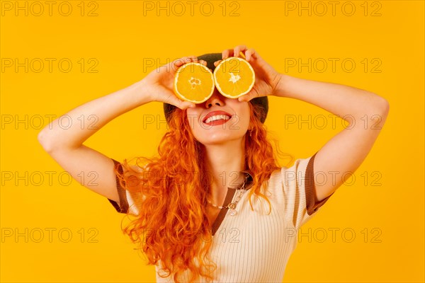 Redhead woman holding an orange over isolated yellow background covering eyes smiling