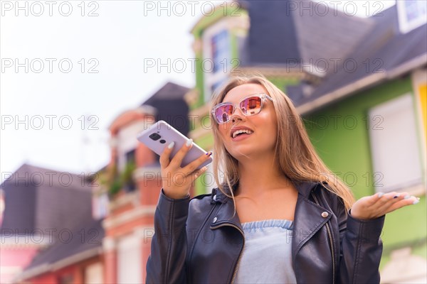 Young blonde woman in a leather jacket sending a voice note with her mobile