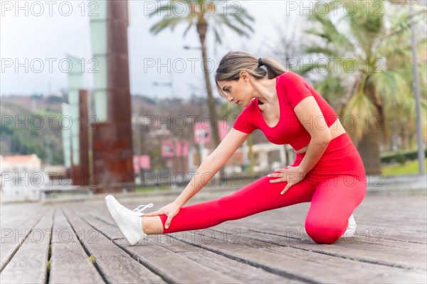 Fit woman in red outfit doing stretching in a city park in spring