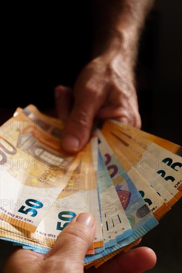 Man's hands handing euro banknotes to woman's hands with black background and copy space