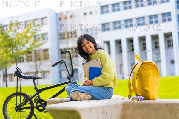 Portrait of a smiling Asian female student sitting in college campus with a bicycle
