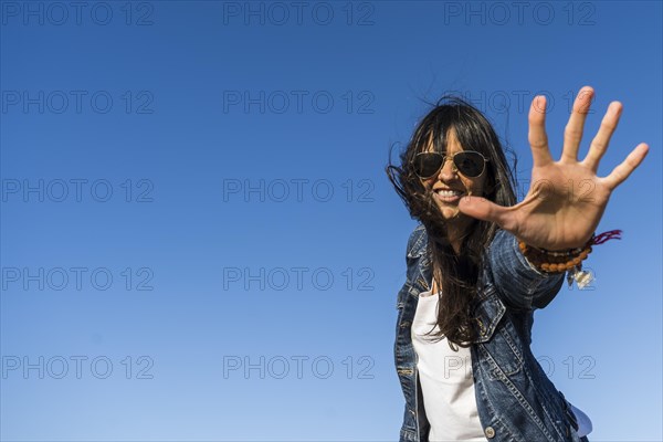 Low angle view of a similing woman while showing her hand. Blue sky background