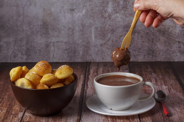 Woman spreading a sugared doughnut with a wooden fork on a hot chocolate in a white mug