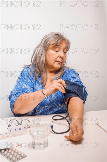 Older white-haired woman with glasses taking her blood pressure at home with white background