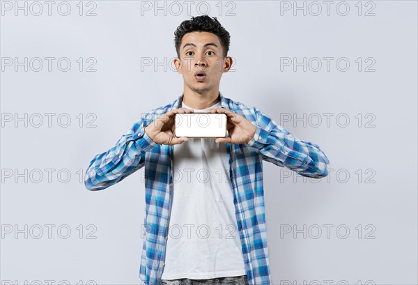 Amazed young man showing ad on cellphone. Surprised handsome man showing the horizontal screen of his cell phone