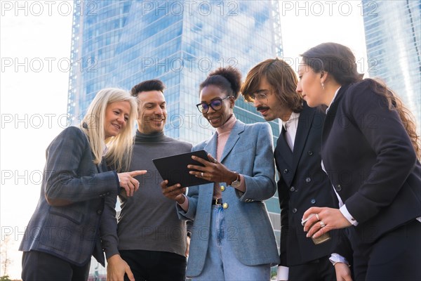A group of smiling multi-ethnic businesspeople looking at a tablet outside the glass building