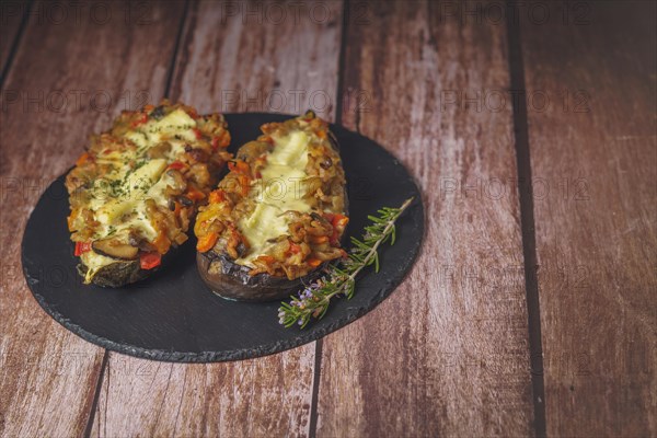 Foreground eggplant stuffed with meat and vegetables covered with bechamel sauce on a black slate on a wooden table