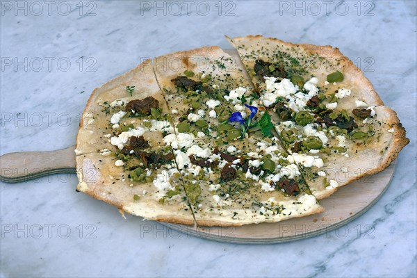 Flammkuchen with olives dried tomatoes and feta cheese on a wooden board
