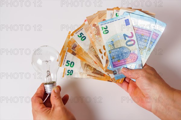 Woman holding banknotes in one hand and a light bulb in the other concept of light prices