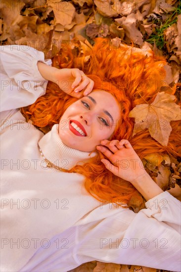 Redhead woman lying on leaves in a forest park