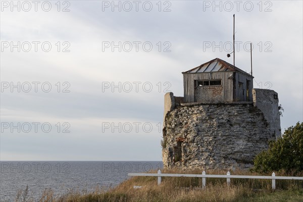 Coastal road and ruins of the historic lighthouse in the evening light on the cliff on Pakri Peninsula