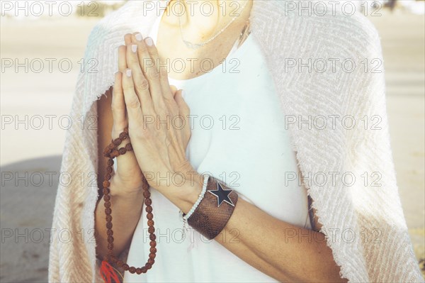 Close up of a woman clasping hands while holding a japa mala outdoors