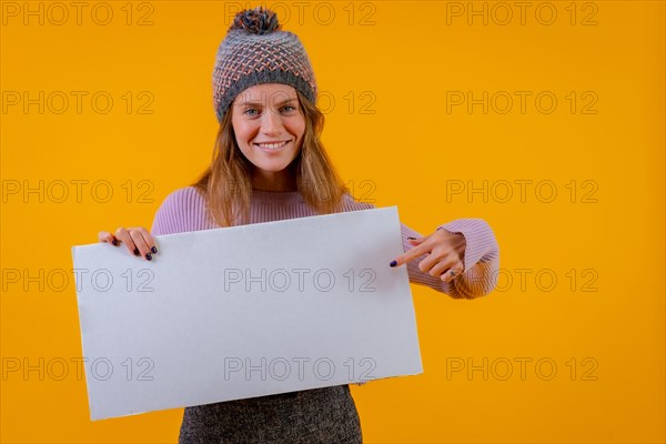 Woman in a wool cap holding a white sign on a yellow background