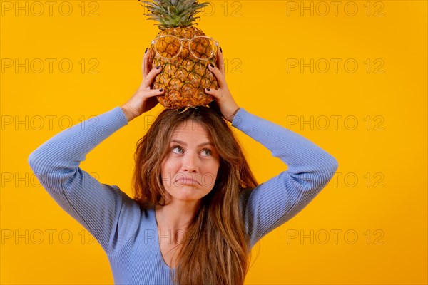 Woman with a pineapple in sunglasses in a studio on a yellow background