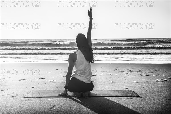 Rearview shot of a young woman practicing yoga at the beach. Black and white photography