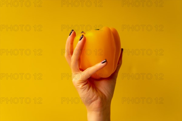 Woman's hand with a vegetable on a yellow background