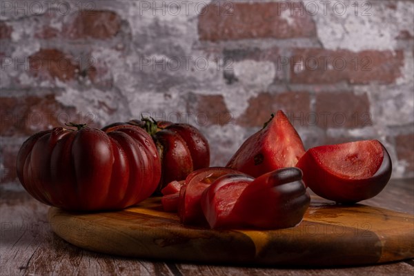 Group of cut and whole organic Moorish tomatoes on a wooden board with a brick wall in the background