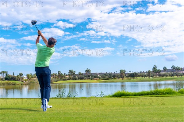 Male golf player on professional golf course. Golfer hitting the ball with driver stick next to a lake