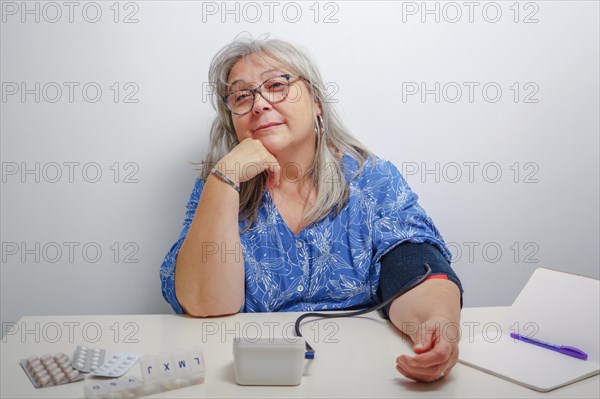 Older white-haired woman with glasses taking her blood pressure at home with white background