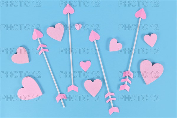 Pink Valentine's day cupid's arrows with heart shaped tips and heart ornaments on blue background