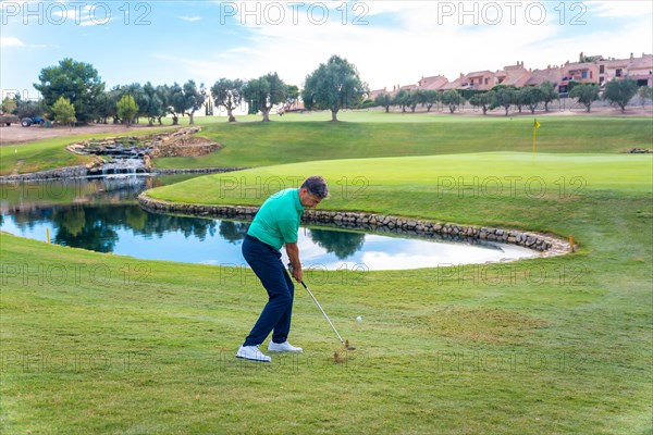 Man playing golf at golf club by a lake