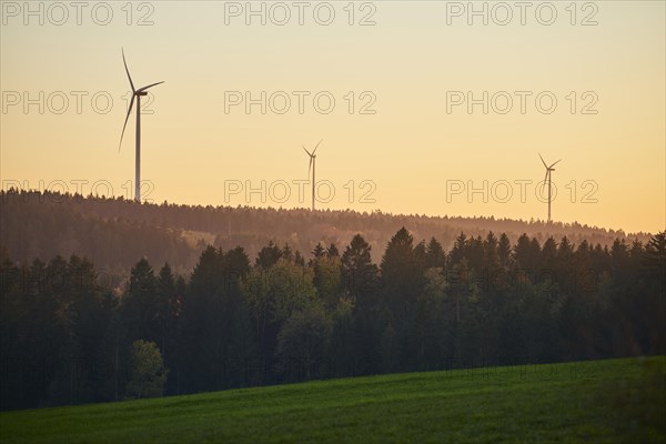 Wind power plants at sunset over a forest in autumn
