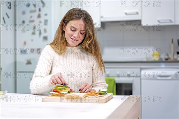 Vegetarian woman cooking a vegetable sandwich in the kitchen at home. Preparing it by putting tomato