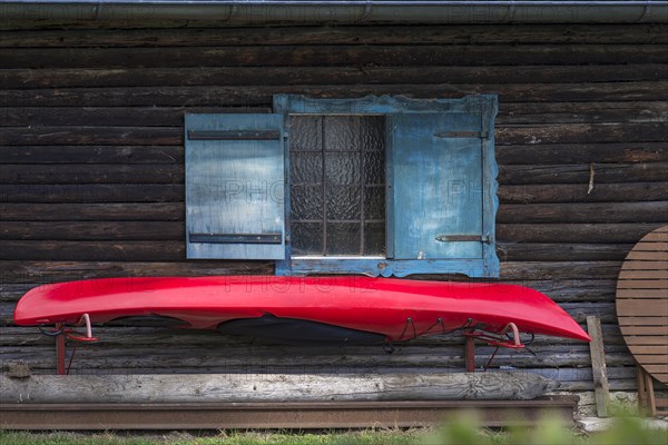 Red kayak boat hanging from a wooden hut with blue shutters