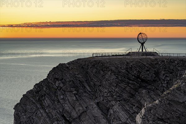 Rock cliff of the North Cape with steel globe at midnight sun