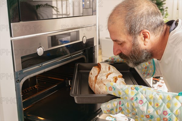Older man with beard putting bread in the oven of his house