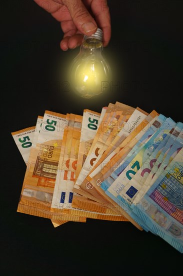 Lighted light bulb with euro banknotes in the background on a black background