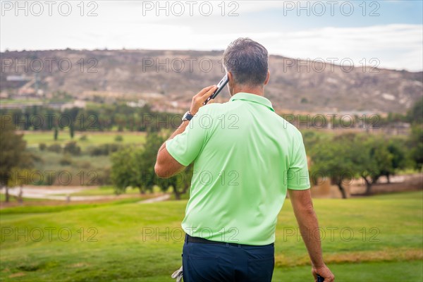 Young businessman playing golf and answering a work call with the phone from the club