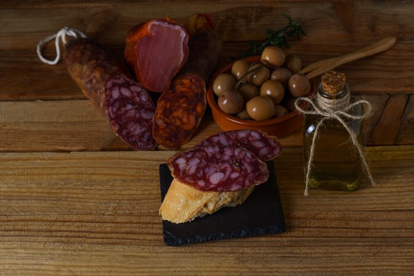 Tapa of iberian sausage on rustic bread with olive oil on a wooden board with black background