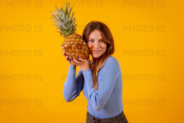 Woman smiling with a pineapple in sunglasses in a studio on a yellow background