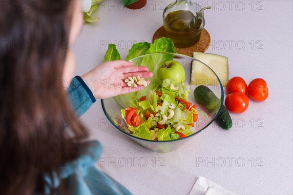 Woman adding cashews to a healthy salad at her kitchen table