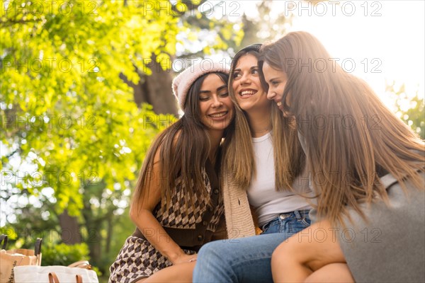 Women friends sitting hugging in a park in autumn at sunset