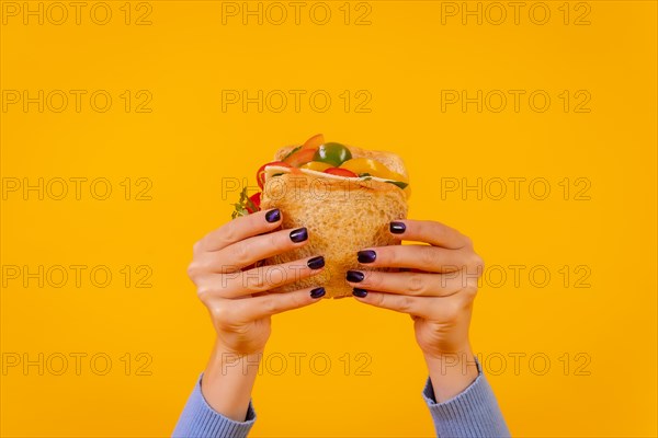 Hands of a woman with a sandwich on a yellow background