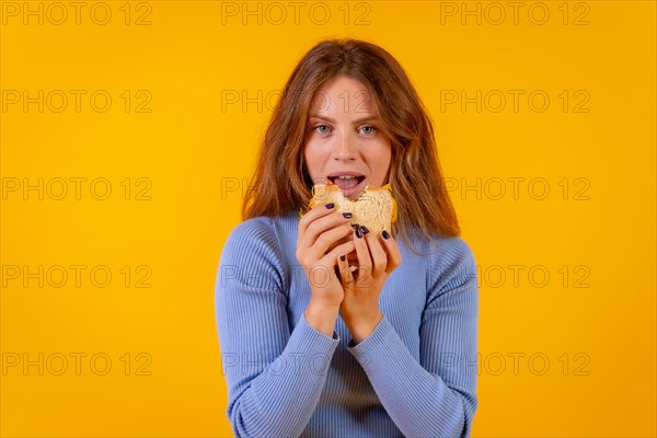 Vegetarian woman eating a sandwich on a yellow background