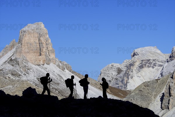 Four mountain climbers silhouetted against Torre dei Scarperi