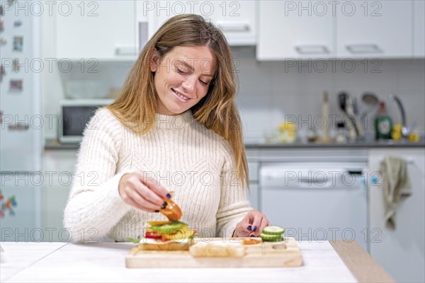 Vegetarian woman cooking a vegetable sandwich in the kitchen at home. Preparing it by putting tomato