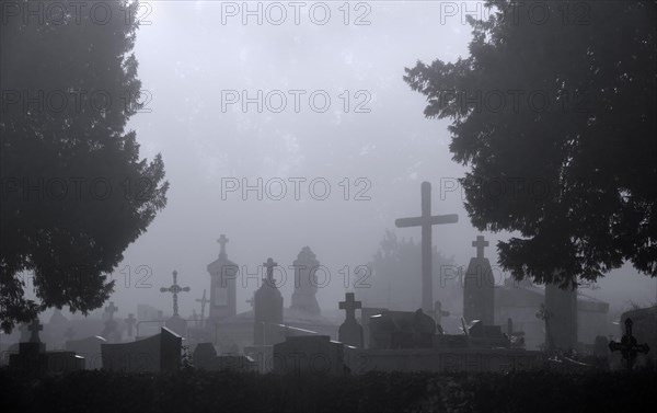 Silhouetted tombs and crosses at graveyard in the mist